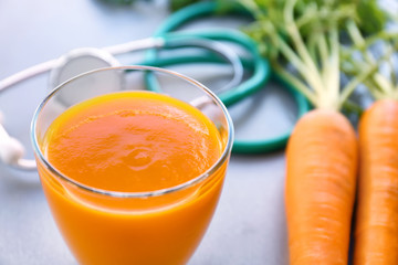 Glass of juice with fresh carrot and stethoscope on grey background. Health care concept