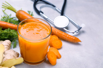 Glass of carrot juice with fresh ginger and stethoscope on grey background. Health care concept