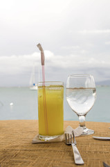 A glass of orange juice and water by the sea