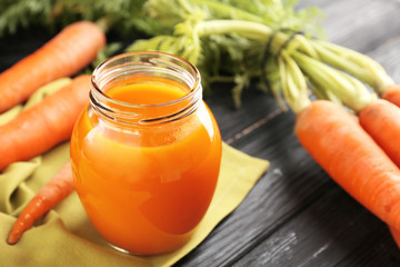 Jar of juice with fresh carrot on wooden background