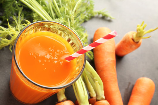 Glass of tasty juice and fresh carrot on grey background