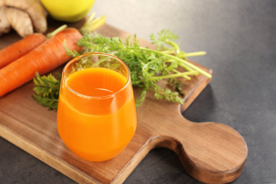 Glass of juice and fresh carrot on cutting board