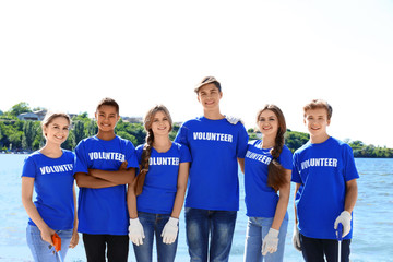 Obraz premium Young people with trash pickers standing on beach near river. Volunteer concept