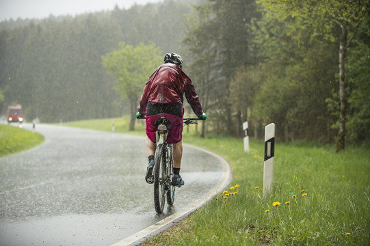 Mann f&auml;hrt auf dem Fahrrad im str&ouml;menden Regen einen Anstieg hinauf