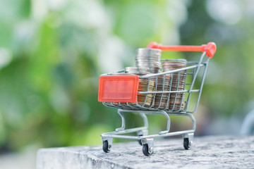 e-commerce, saving and shopping concept. Stack of coins in mini shopping cart with green nature background.