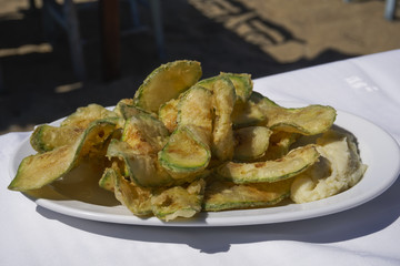 Fried zucchini chips with garlic mash served on a white dish by the beach.
Fried zucchini with scordalia recipe, greek potato and garlic dip, on on white linen tablecloth.