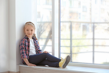 Smiling girl sitting on sill near big window