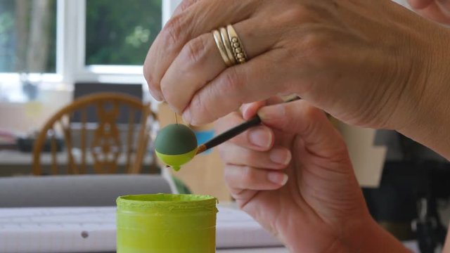 elderly artiest making arts and crafts necklace, painting polymer clay bead with brush in studio