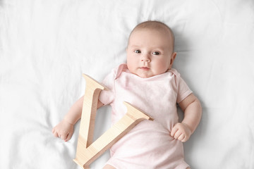Cute baby with letter V lying on bed. Choosing name concept