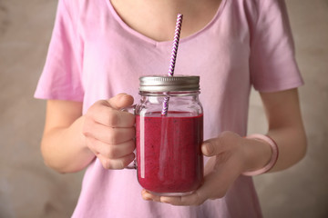 Young woman holding mason jar of fresh berry yogurt smoothie on grey background, closeup