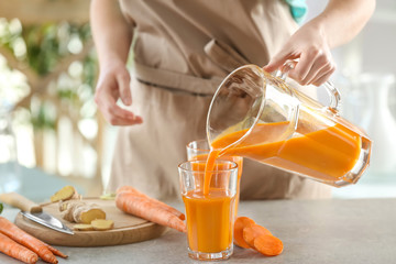 Jeune femme remplissant un verre de jus de carotte frais dans la cuisine