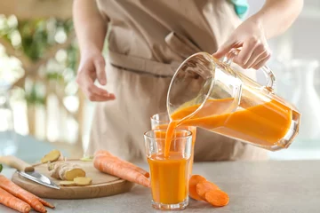 Cercles muraux Jus Jeune femme remplissant un verre de jus de carotte frais dans la cuisine