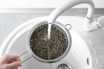 Poster Im Rahmen Washing raw lentils with tap water before cooking in kitchen © Africa Studio