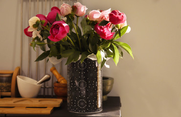 Vase with bouquet of beautiful peonies on table in kitchen