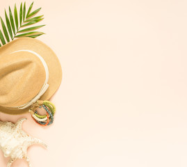 Summer fashion, summer outfit on cream background. Seashell, wood bracelet and straw hat. Flat lay, top view.
