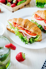 Breakfast, business lunch, sandwiches croissant with ham, cheese, sauce, lettuce, tomato and strawberry mint ice-cold cocktail on a light background 