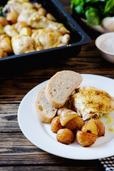 Hearty and delicious dinner, baked chicken legs and thighs with potatoes, onions, tomatoes, spices, herbs and white bread on a dark wooden background