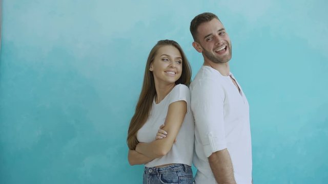 Young couple standing back to back flirting each other and turn for kiss on blue background