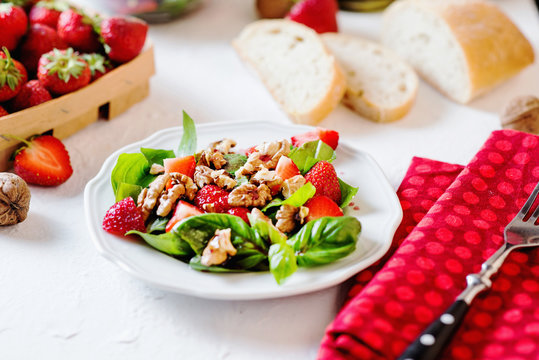 Fresh summer salad with strawberries, basil, walnuts with olive oil sauce and balsamic vinegar with white bread on a light background 