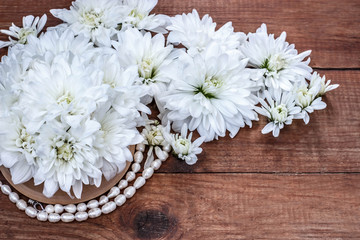 a bouquet of white chrysanthemum and pearls on a brown wooden background