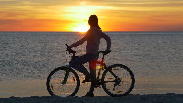 Woman on bicycle looking at sunset over the sea