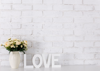 white wooden word love, flowers and space over white brick wall