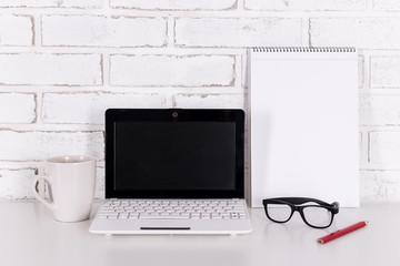 white modern laptop, glasses and notebook on the table