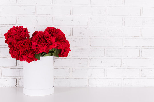Red Flowers In Vase Over White Brick Wall