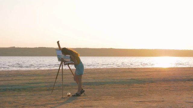 Young woman artist painting landscape in the open air on the beach