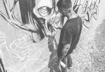Obraz na płótnie Canvas Tattoo graffiti writer painting with color spray his dark picture on the wall - Contemporary artist at work - Urban lifestyle,street art concept - Black and white editing - Vintage retro filter