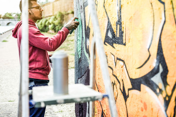 Tattoo graffiti writer painting with color spray on the wall - Contemporary artist at work - Urban lifestyle,street art concept - Focus on his face and hand can