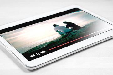 Online movie stream with mobile device. White tablet on wooden table with imaginary video player...