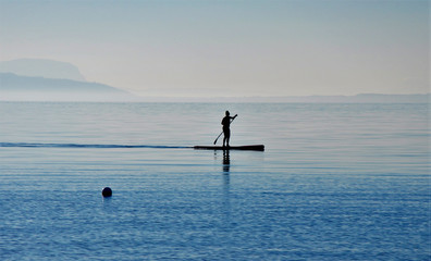 The woman on the board with a paddle floating on a calm sea sup.