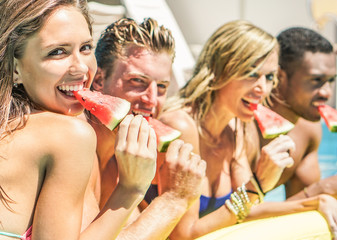 Happy friends eating watermelon in swimming pool hotel resort - Diverse culture couples having fun in summer vacation - Travel, youth, holidays concept - Focus on left girl - Warm contrast filter