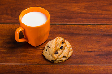 An orange glass of milk with a chocolate cookie baked with stevia on wooden background