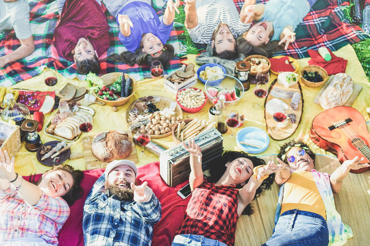 Top view of happy friends at picnic on city park outdoor - Young having fun at bbq dinner in summer time - Focus on bottom guys hands  - Food , vacation and friendship concept - Warm retro filter