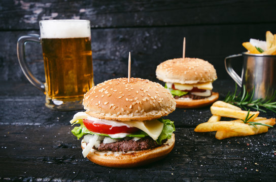 Hamburger with french fries, beer on a burnt, black wooden table. Fast food meal. Homemade hamburger consist of beef meat, lettuce, tomato, bins, dressing, cheese and spices. Vintage 
