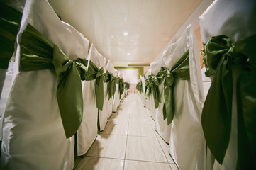 a number of the white wedding chairs decorated with a green bow, background