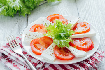 Feta cheese slices with tomato on white plate  