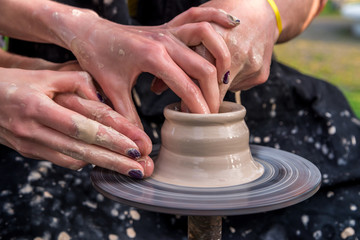 Pottery. Men's hands make a clay jug or pot on the machine. He is helped by women's hands. A man in a dressing gown, spattered with clay. Horizontal frame