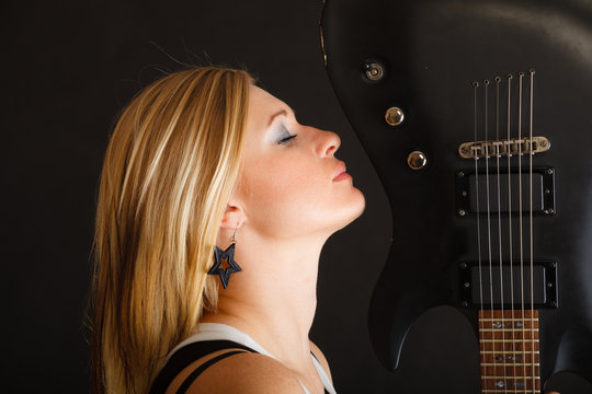 Blonde woman holding electric guitar, black background
