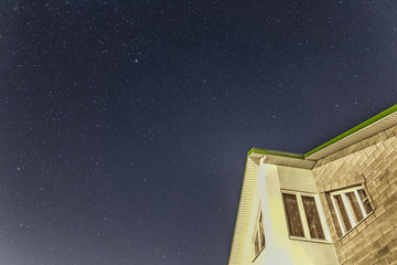 Starry sky over the roof of suburban house. Background with millions of stars over the mansard.