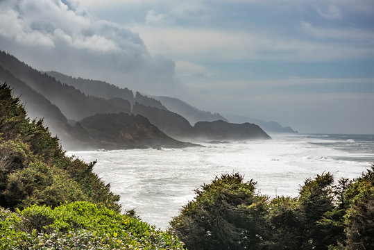 Stormy coastline in Oregon with fog and white ocean beach with cliffs and forests