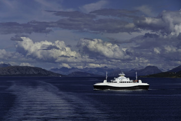 Fototapeta na wymiar Passing the ferry Heroysund near Bronnysund, Norway, under storm clouds, with mountains in background