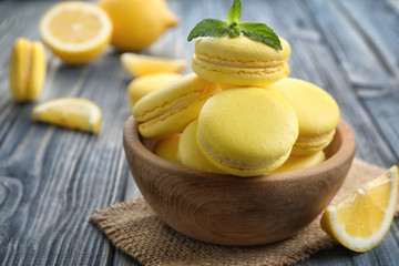 Wooden bowl with tasty lemon macarons on wooden table, closeup