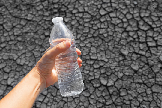 Water saving concept. Hand holding bottle of water over a dry river bed.  