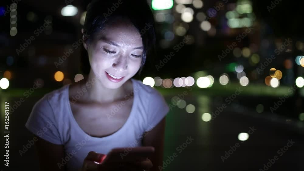 Wall mural young woman using cellphone at night