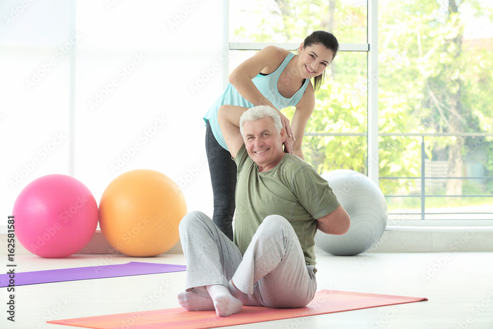 Sticker Instructor helping senior man to practice yoga in gym