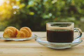 A cup of coffee and croissants on blurred green natural background, selective focus and vintage retro color