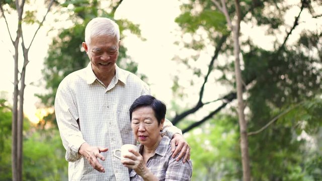 Asian senior couple showing affectionate and care through a cup of coffee in morning bright natural park